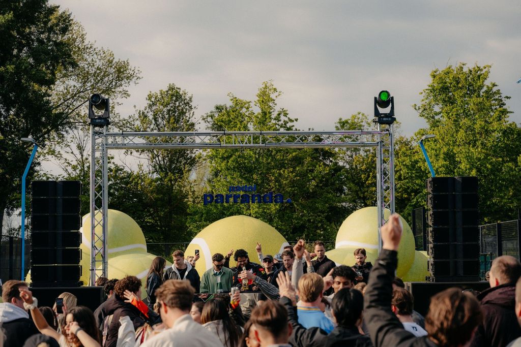Volle Wiese vor der Bühne bei Padel Parranda Amsterdam, darüber der Schriftzug, daneben Riesen-Tennisbälle
